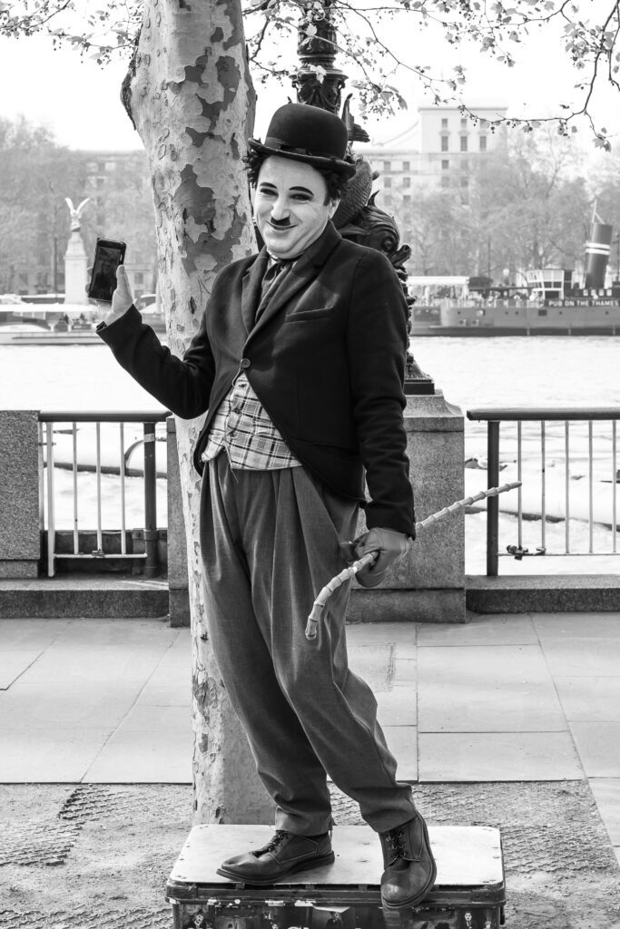 Home Black and white photo of a street performer dressed as Charlie Chaplin on a London riverside.